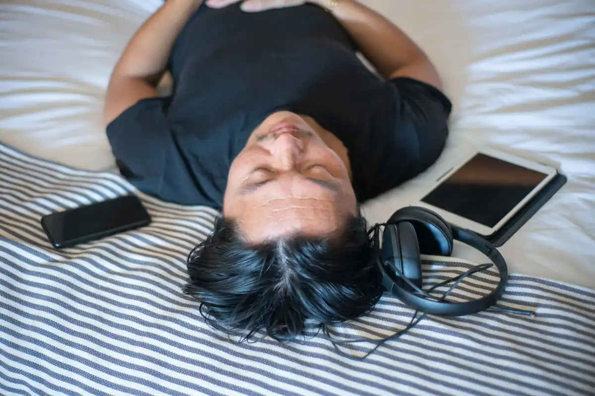 Bărbat relaxat cu ochii închiși, înconjurat de telefon, tabletă și căști