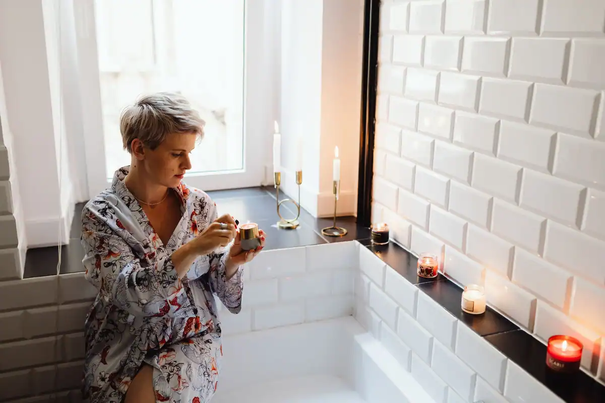 Femeie în halat care aprinde lumânări parfumate înainte de o baie relaxantă