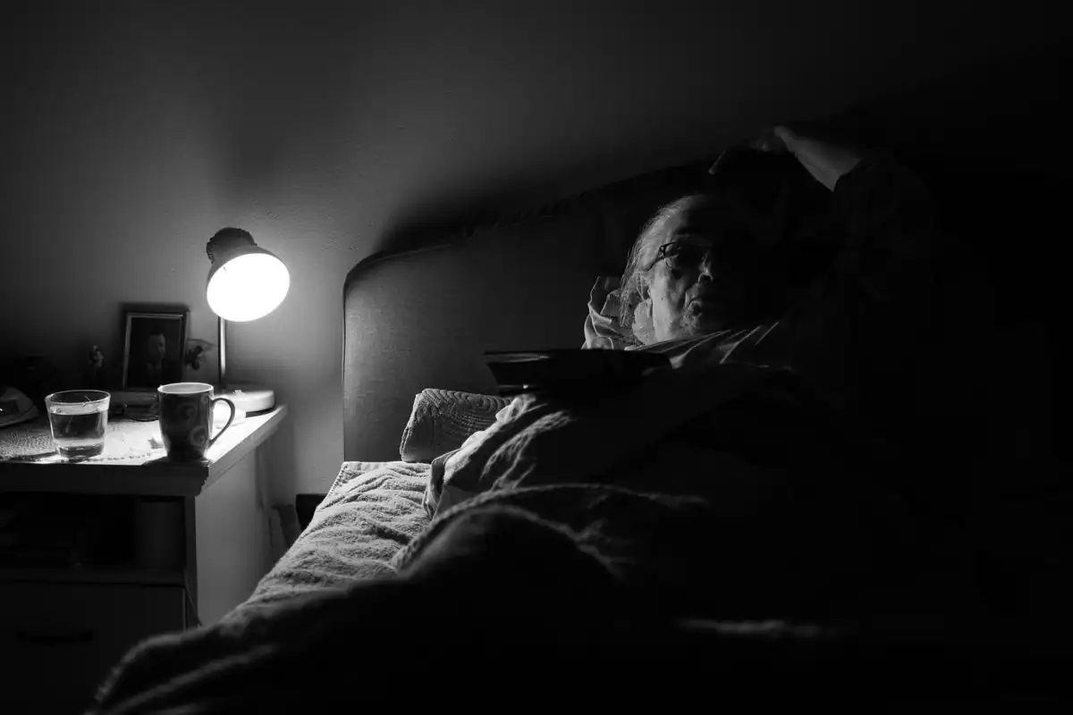 Femeie în vârstă întinsă în pat sub lumina unei veioze, pregătindu-se de somn