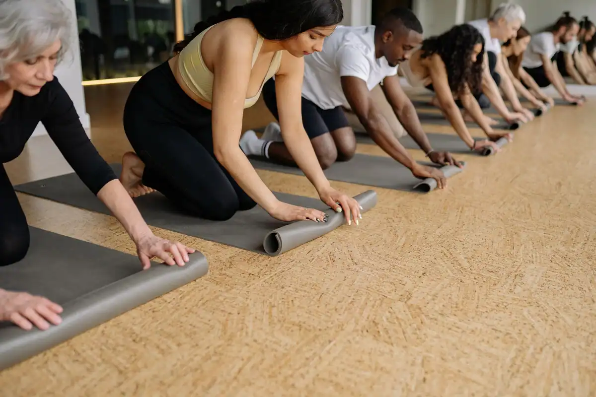 Grup de adulți care își rulează saltelele de yoga într-o sală luminoasă înainte de practică