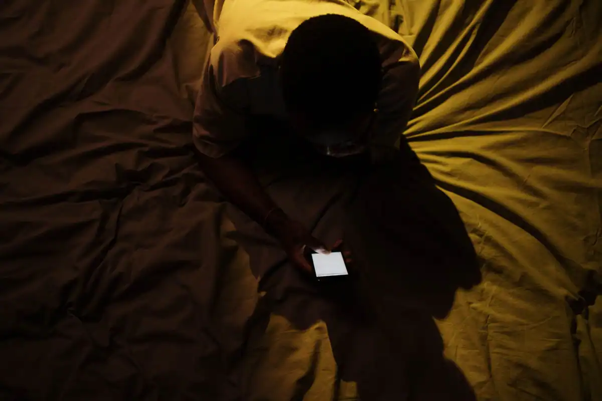 Persoană care folosește telefonul în pat, în lumina slabă dinaintea culcării