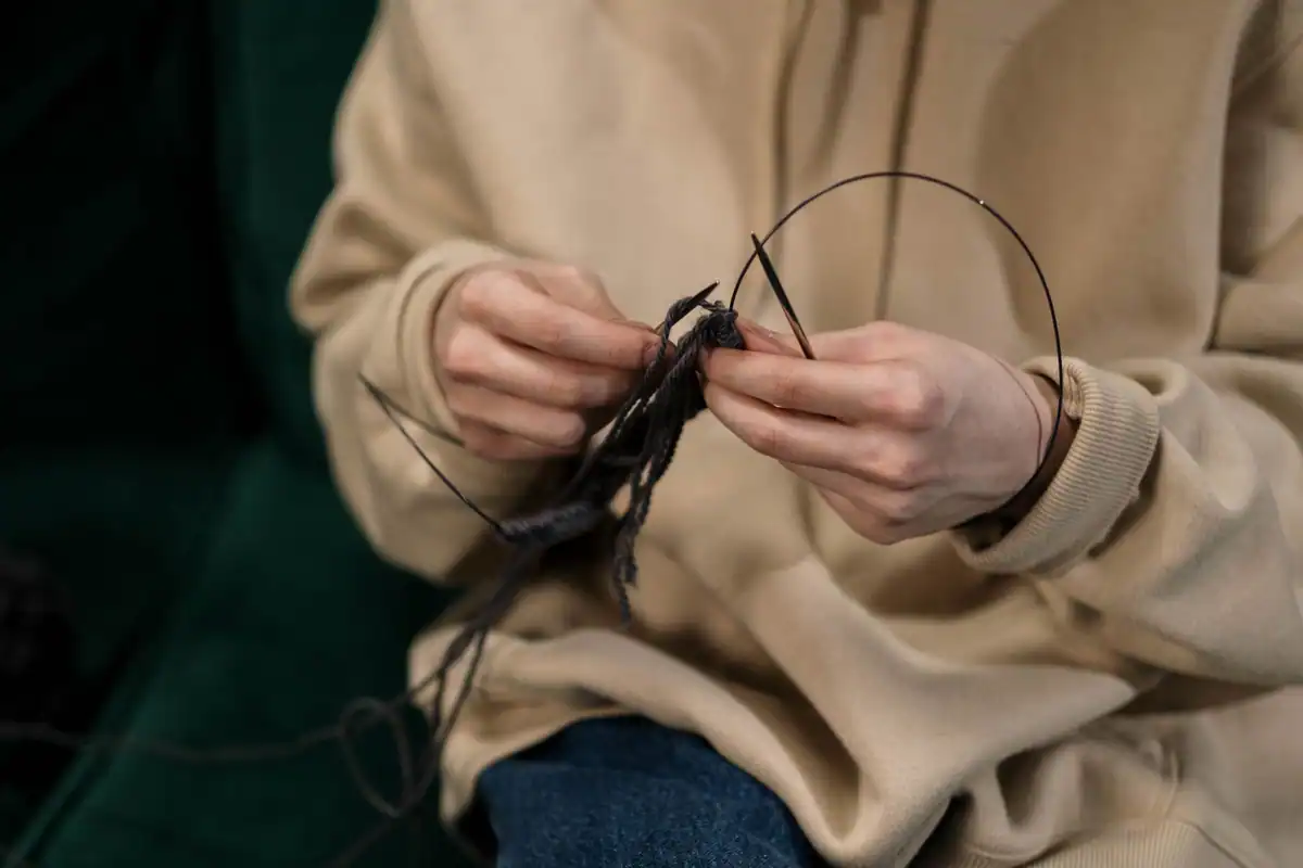 Mâini care tricotează cu fir negru, un hobby manual liniștitor în casă