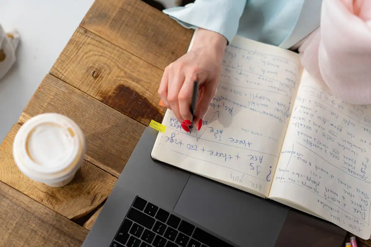 Femeie care notează gânduri într-un carnet, cu o cană de cafea alături pe masa de lemn