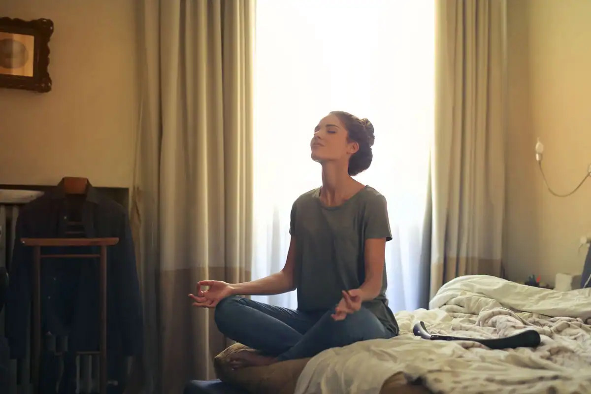 Femeie adultă care practică meditația pe pat, într-un dormitor calm