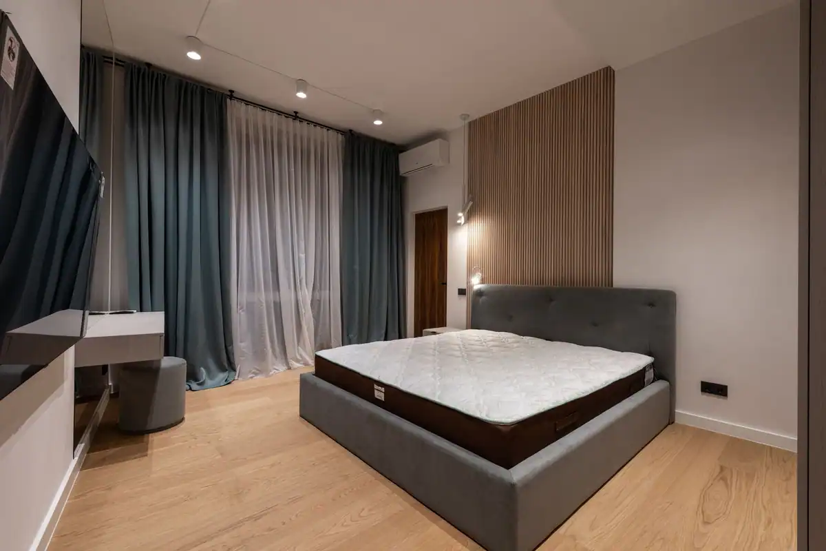 Dormitor modern cu pat confortabil, veioze și draperii, plus un televizor pe perete