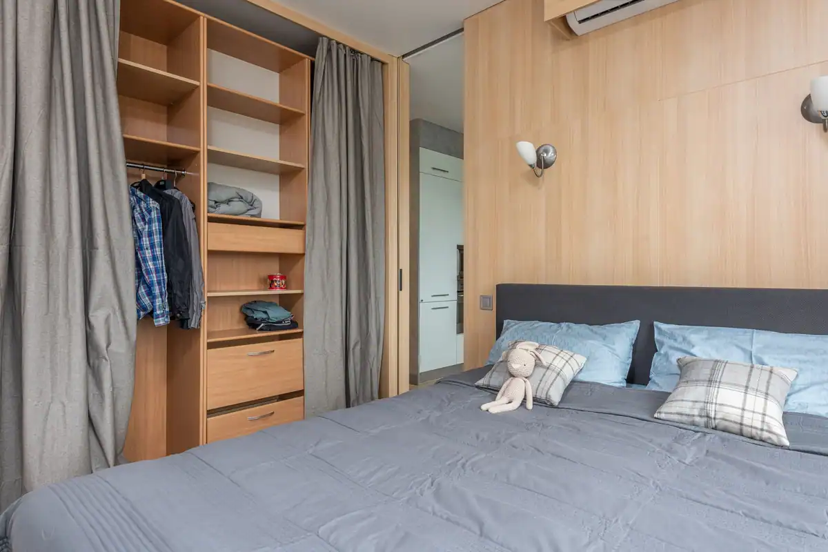 Interior modern luminos, cu pat cu perne, iepuraș de pluș, dulap din lemn, perdele și rafturi