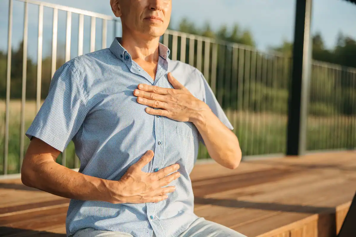 Bărbat cu o mână pe piept și una pe abdomen, exersând respirația în aer liber