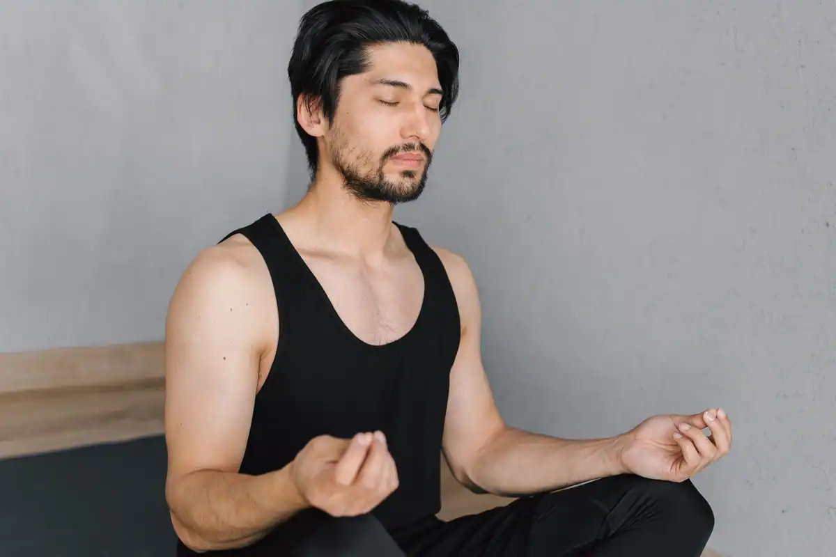 Tânăr cu barbă care stă în poziția lotus cu ochii închiși, respirând ritmic
