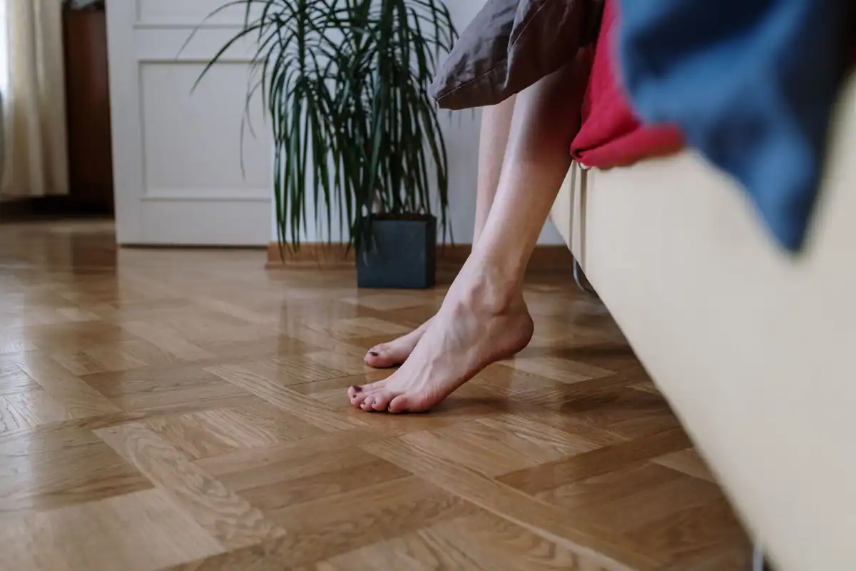 Tălpi goale pe podeaua de lemn, cu plante verzi în fundal