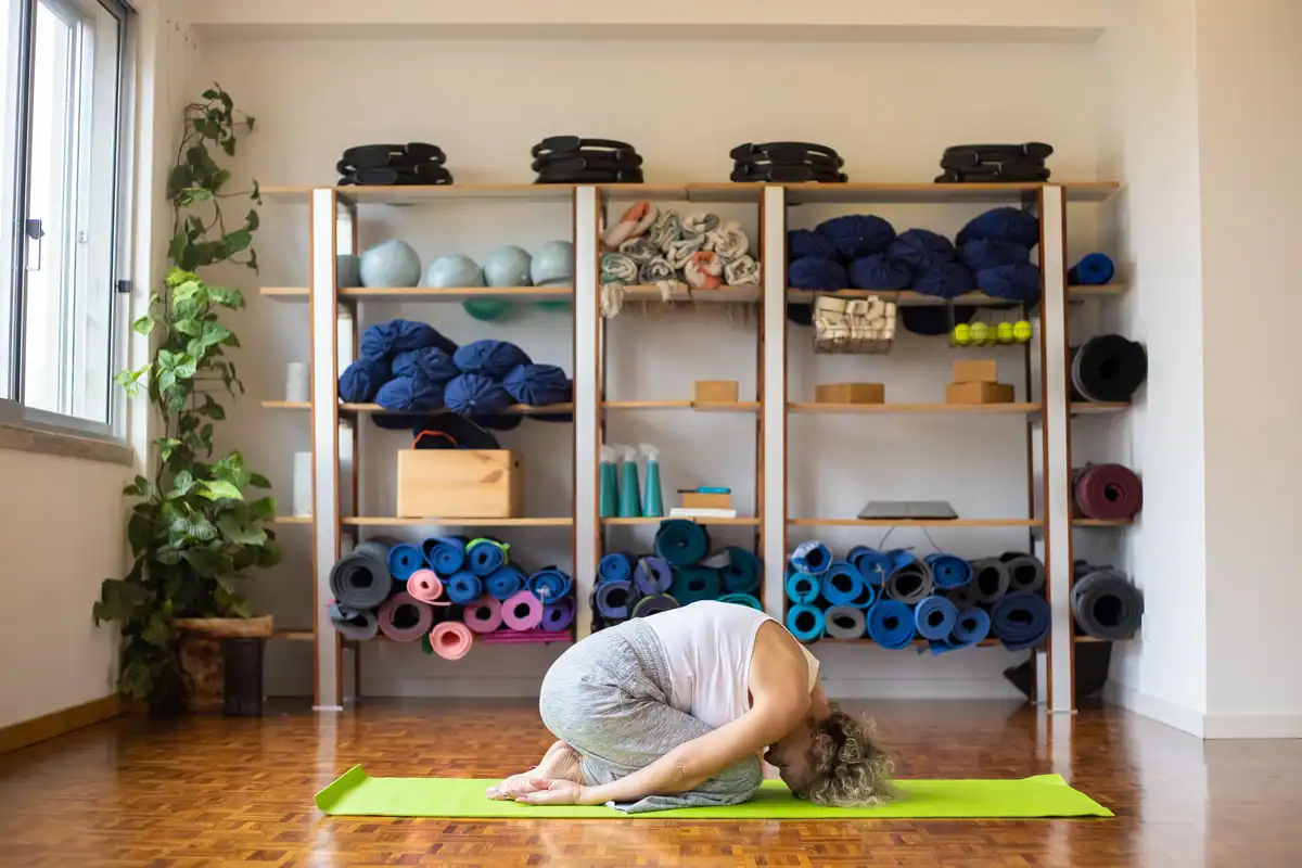 Femeie care face yoga pe saltea într-o sală dotată cu accesorii și lumină naturală