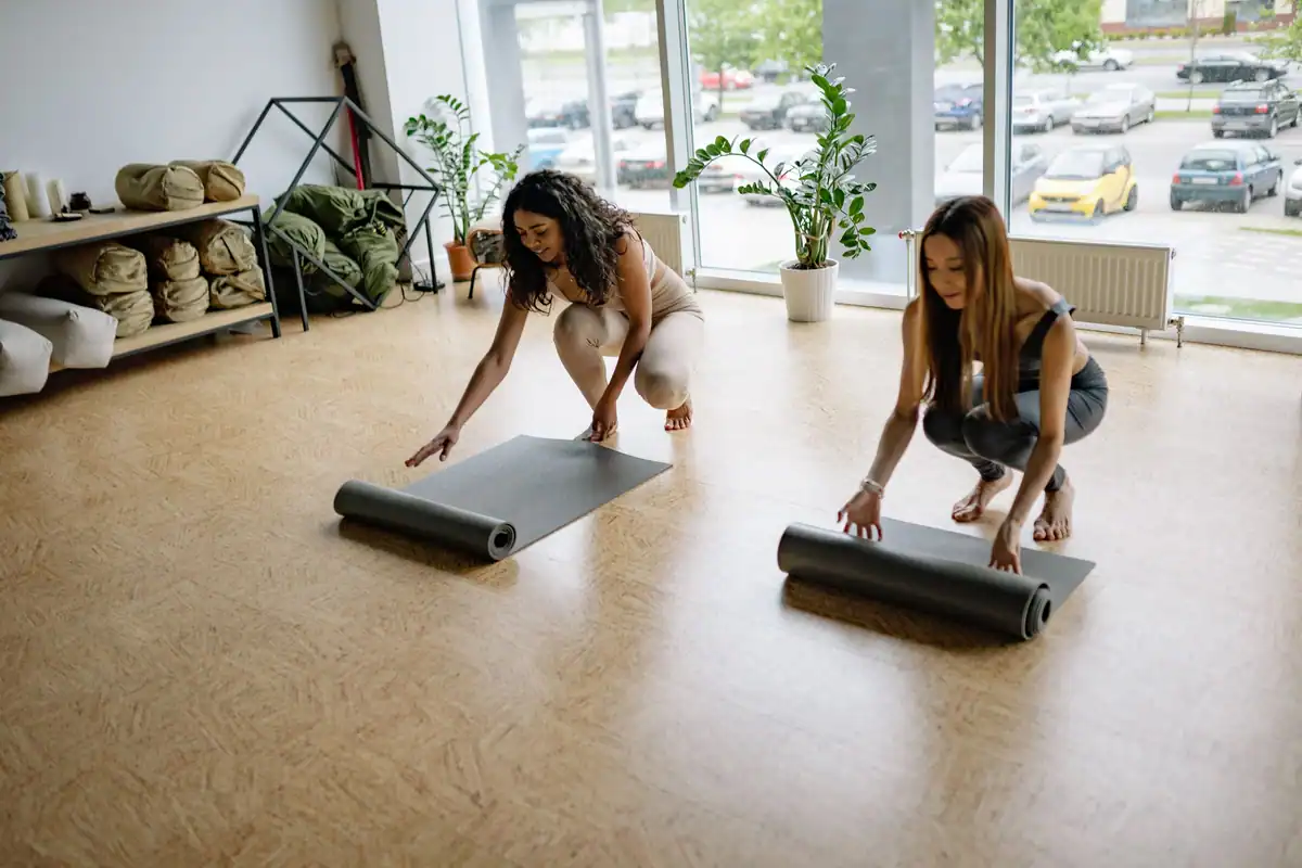 Două femei care își desfac saltelele de yoga într-o sală însorită