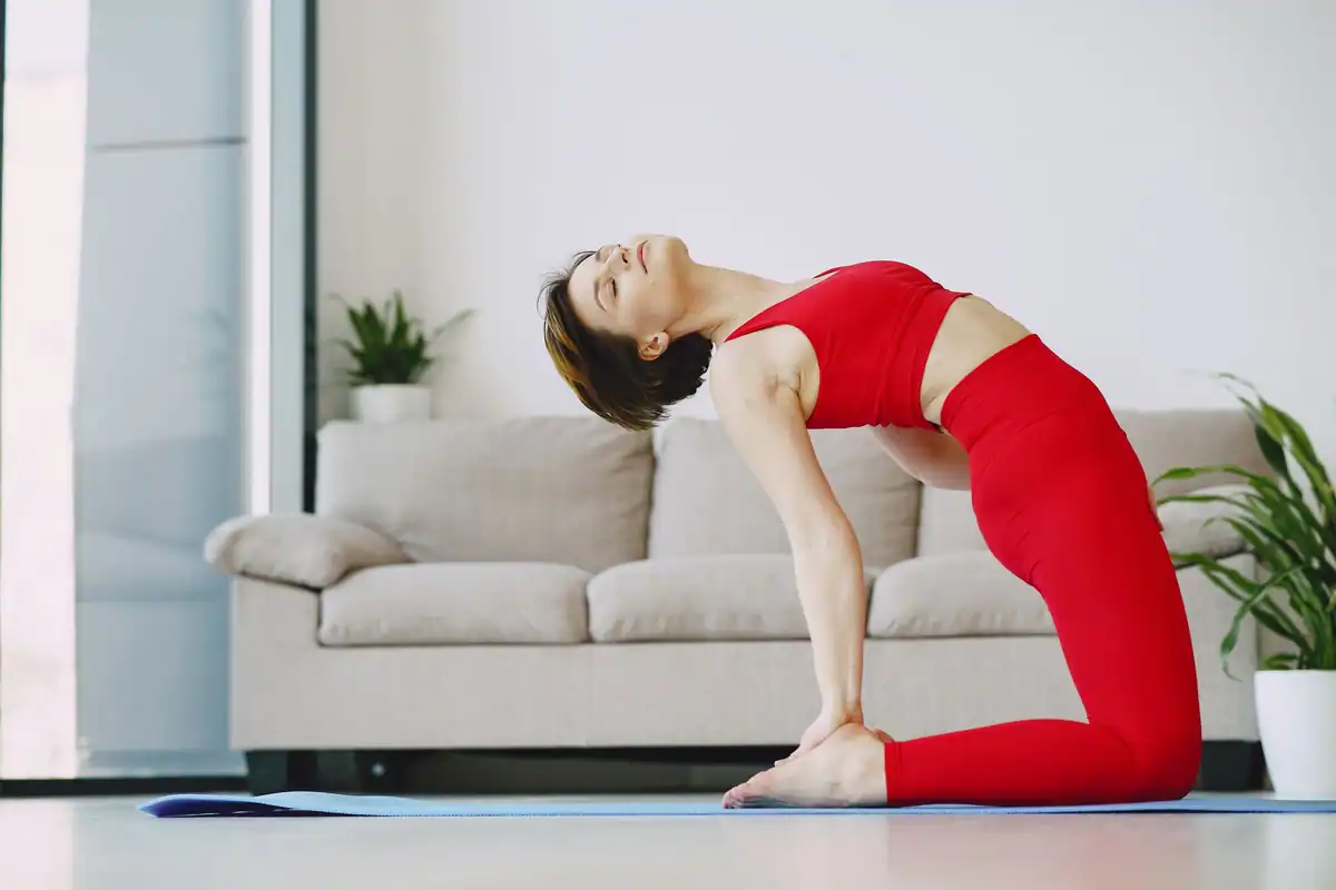 Sportivă cu ochii închiși care face yoga acasă pe saltea, lângă canapea