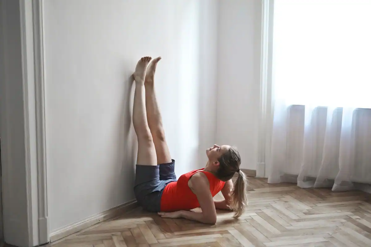 Femeie care face o întindere de yoga cu picioarele sprijinite vertical pe perete