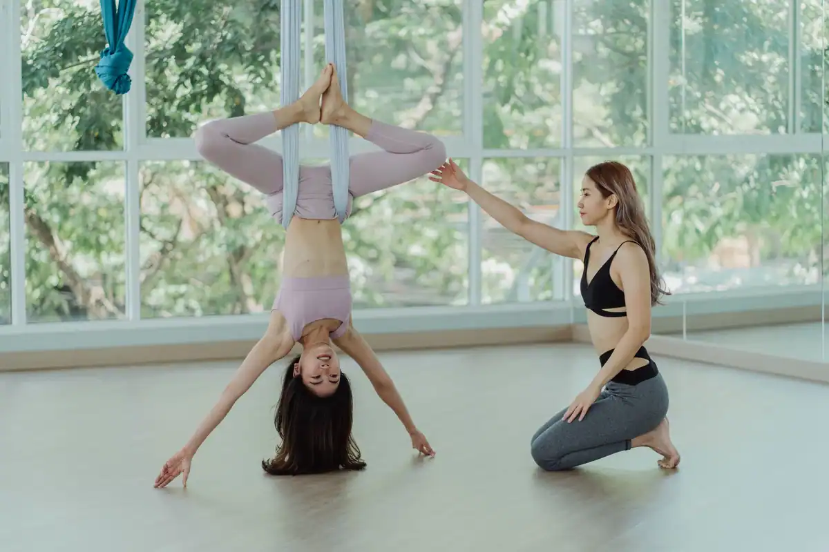 Instructor care ajută o cursantă la yoga aeriană, atent la siguranța ei